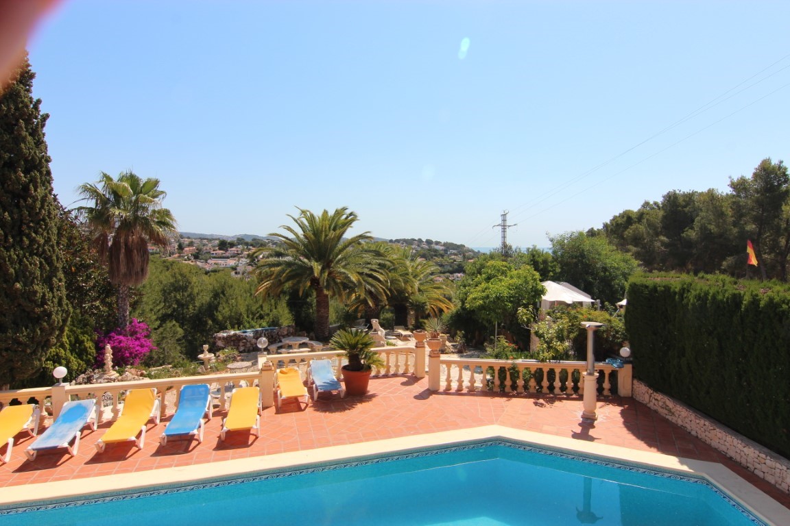 Weitläufige Poolterrasse mit Terrakotta-Fliesen, Sonnenliegen und klassischer Balustrade, umgeben von mediterraner Vegetation und Blick auf das Meer.