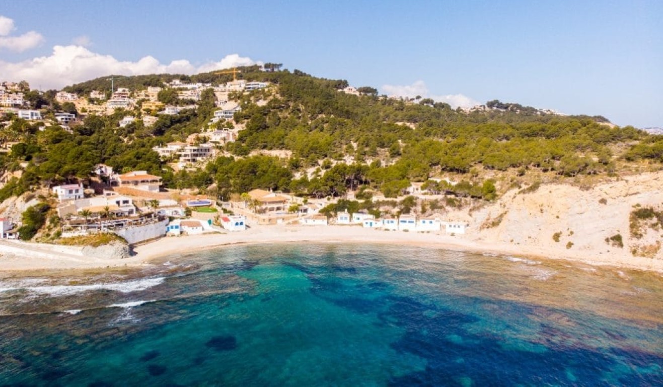 Luftperspektive der Bucht von Portichol mit traditionellen weißen Häusern, türkisfarbenem Mittelmeerwasser und der zerklüfteten Küste von Jávea.