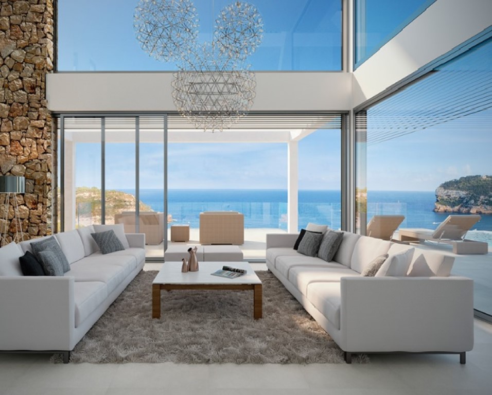 Doppelstöckiger Wohnbereich mit bodentiefen Glasfronten, Natursteinwand und Designer-Leuchten. Panoramablick auf das Meer und Zugang zur Terrasse.