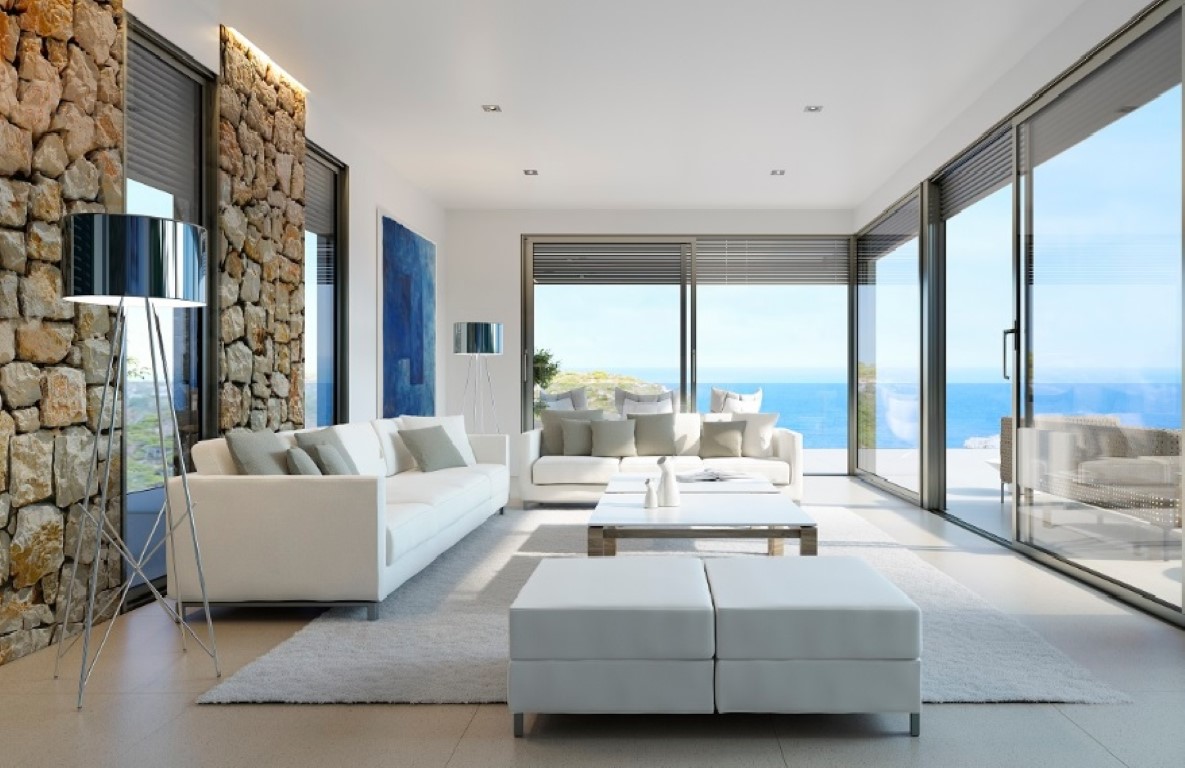 Helles Wohnzimmer mit weißen Sofas, einer Natursteinwand mit LED-Beleuchtung und bodentiefen Glasfronten mit weitem Meerblick.