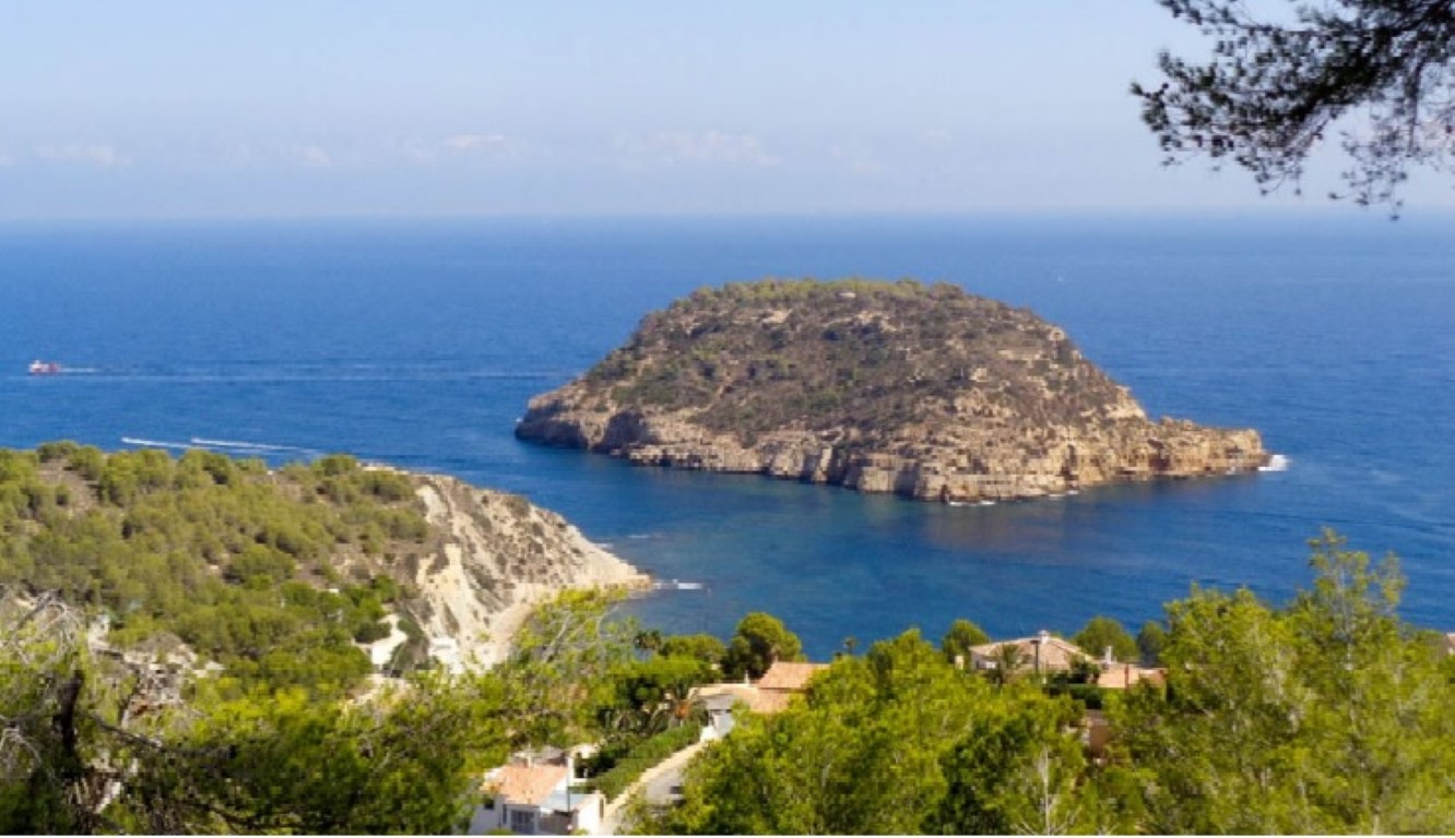 Panoramablick auf das Mittelmeer und die Insel Portitxol, eingerahmt von einheimischen Pinien und mediterraner Küstenlandschaft.