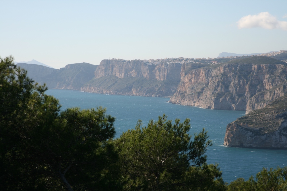 Panoramablick auf das Mittelmeer und die Küstenfelsen von Javea, eingerahmt von einheimischen Pinien von der erhöhten Lage der Baugrundstücke aus.