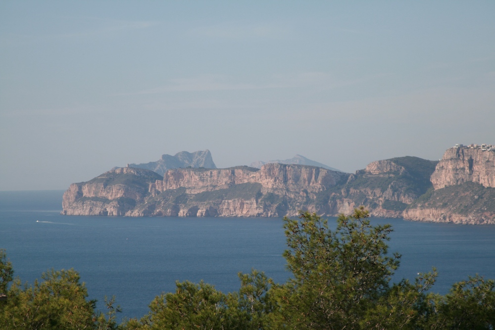 Panoramablick auf das Mittelmeer und die zerklüfteten Kalksteinfelsen von Javea, eingerahmt von einheimischen Pinien unter klarem Himmel.