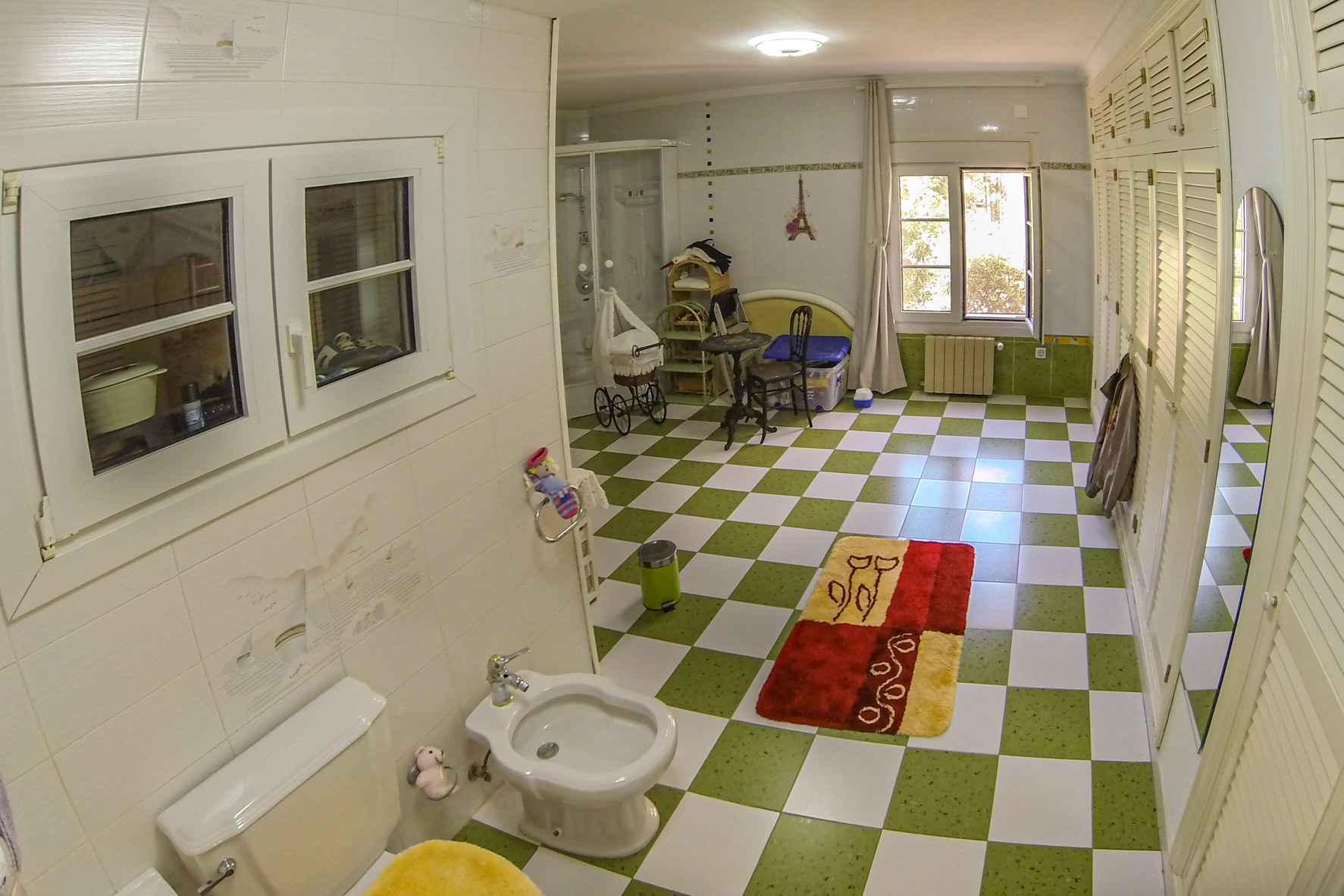 Badezimmer mit grün-weiß gefliestem Boden, weißer Toilette und Bidet sowie einem Fenster mit Tageslicht.