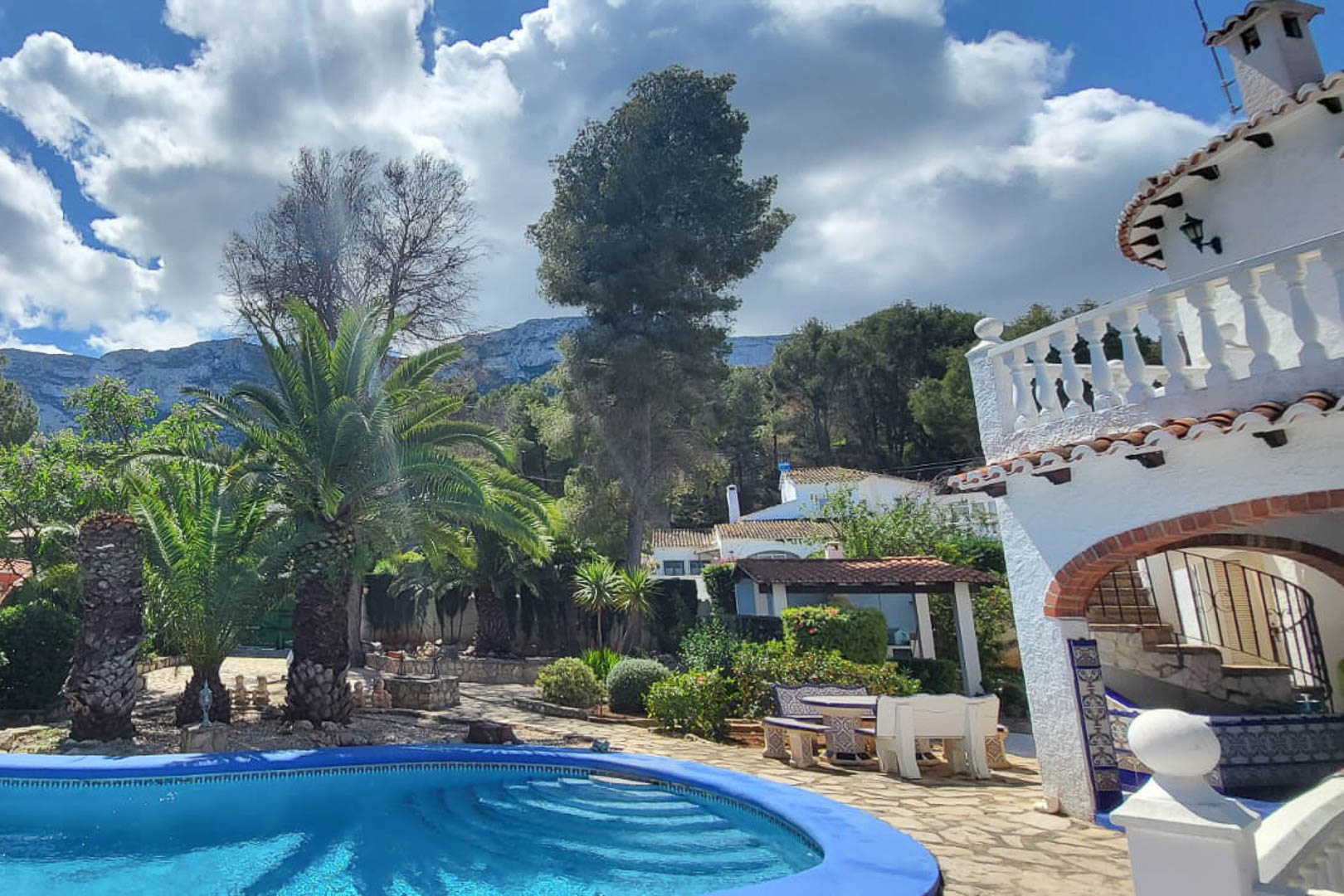 Blick auf den blauen Pool mit Stufenzugang, umgeben von Gärten und dem Haupthaus in Denia.