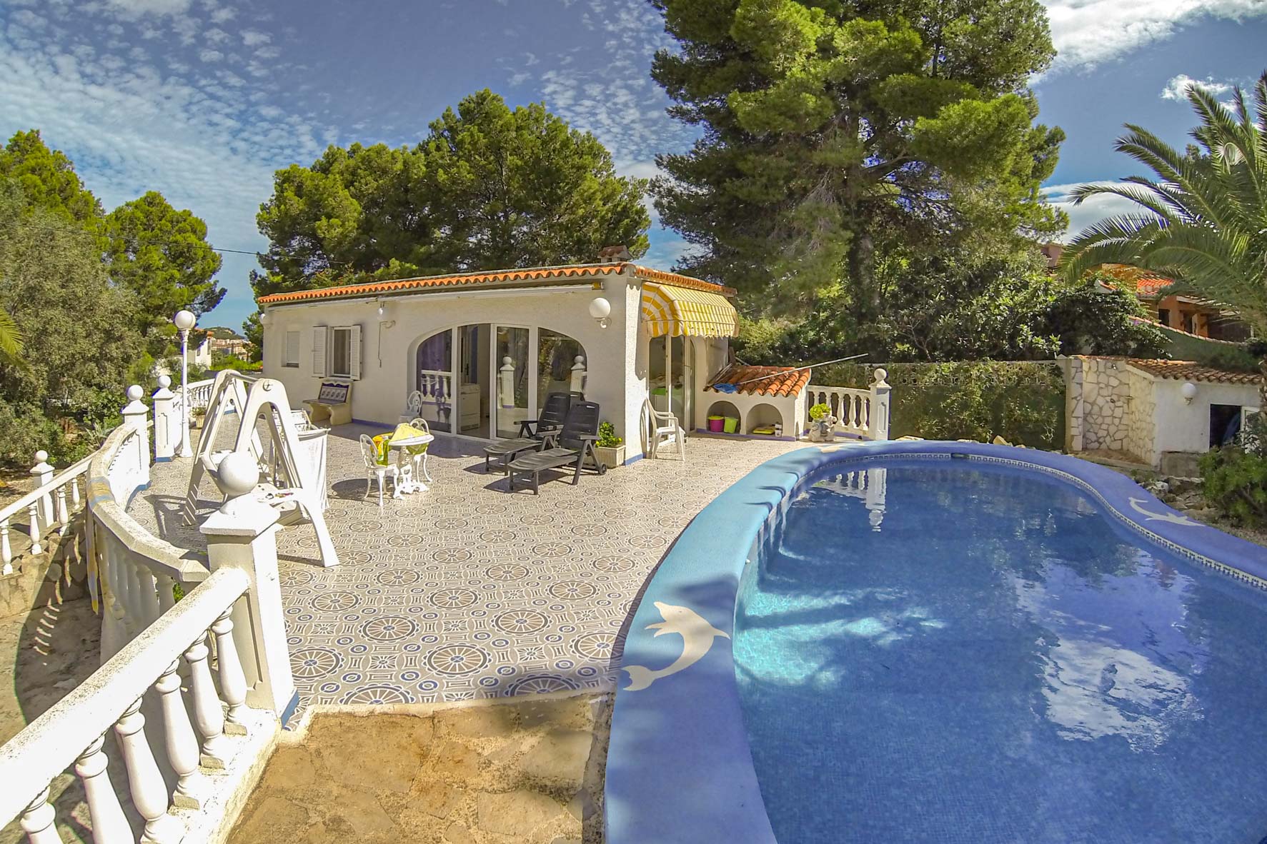 Blick auf den privaten Pool mit blauen Mosaikfliesen und das Poolhaus mit gelber Markise.
