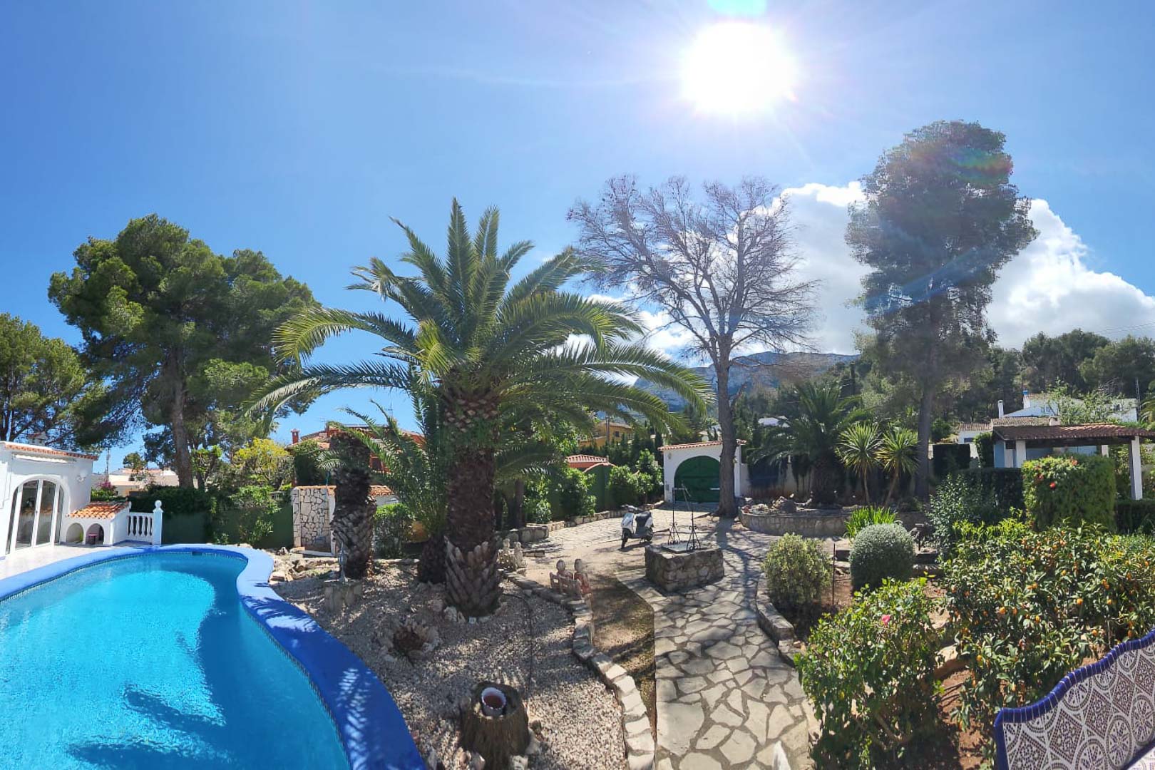 Blick auf den türkisblauen Pool und die Gärten mit Palmen und Steinweg in Denia.