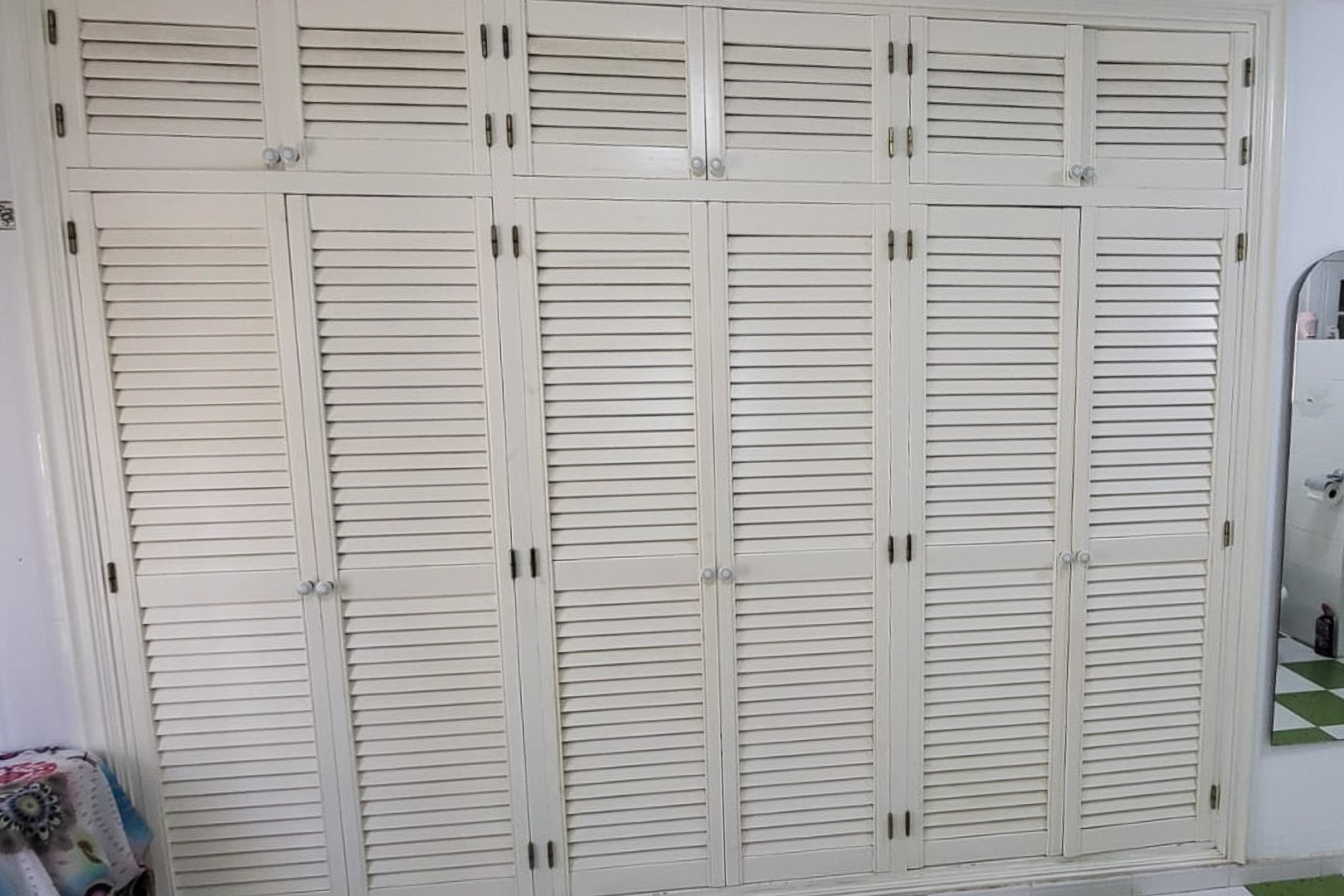 Einbauschrank aus Holz mit Jalousietüren und runden Knöpfen, der die gesamte Wand einnimmt.