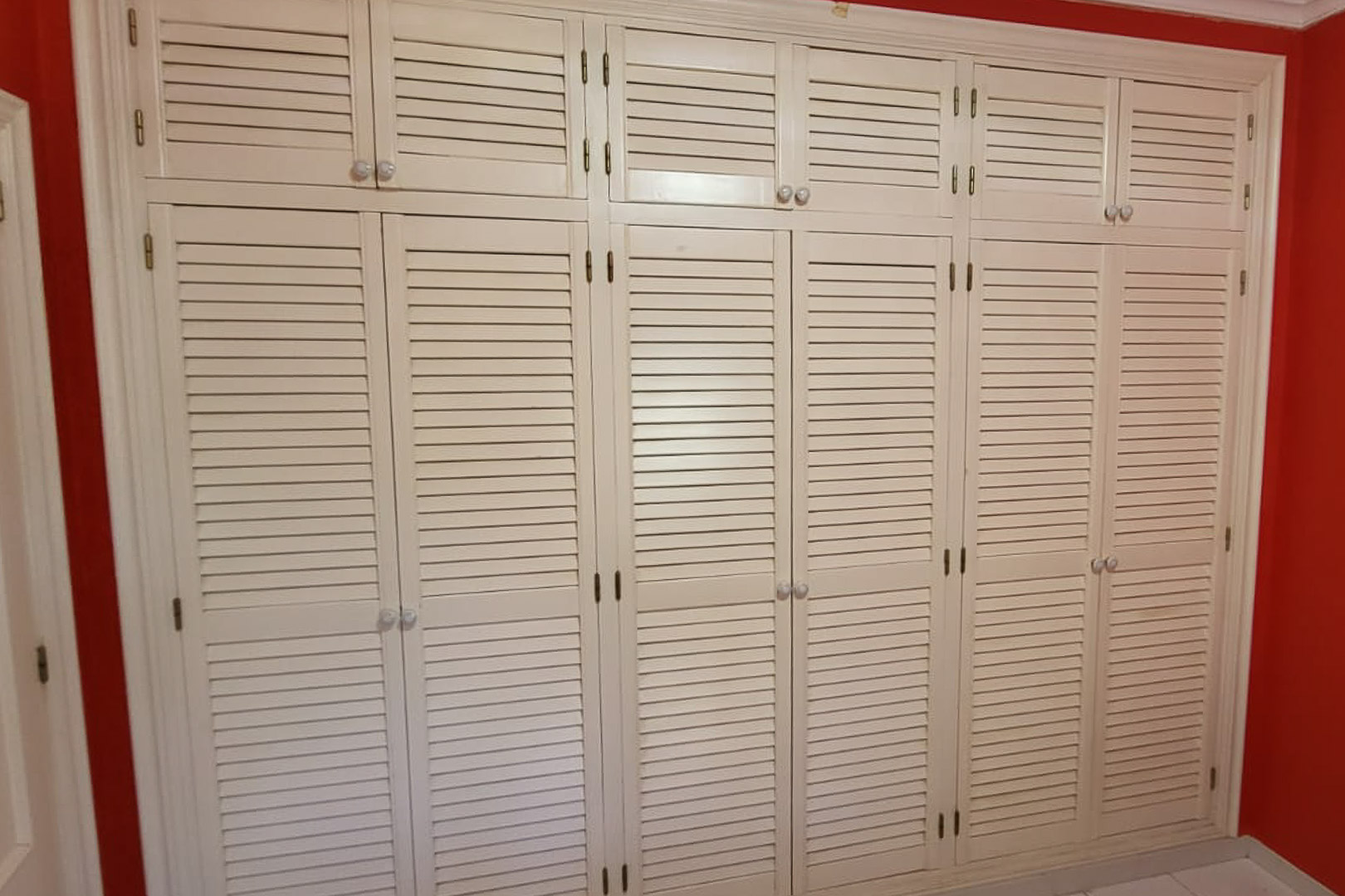 Einbauschrank mit Lamellentüren in Schlafzimmer mit roter Wand.