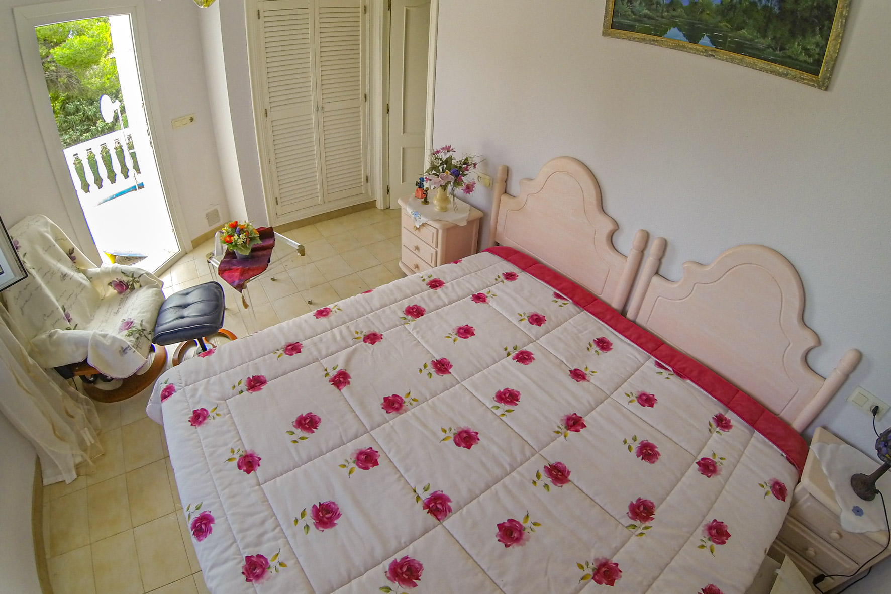 Helles Schlafzimmer mit Doppelbett, floraler Bettwäsche und Zugang zur Terrasse.