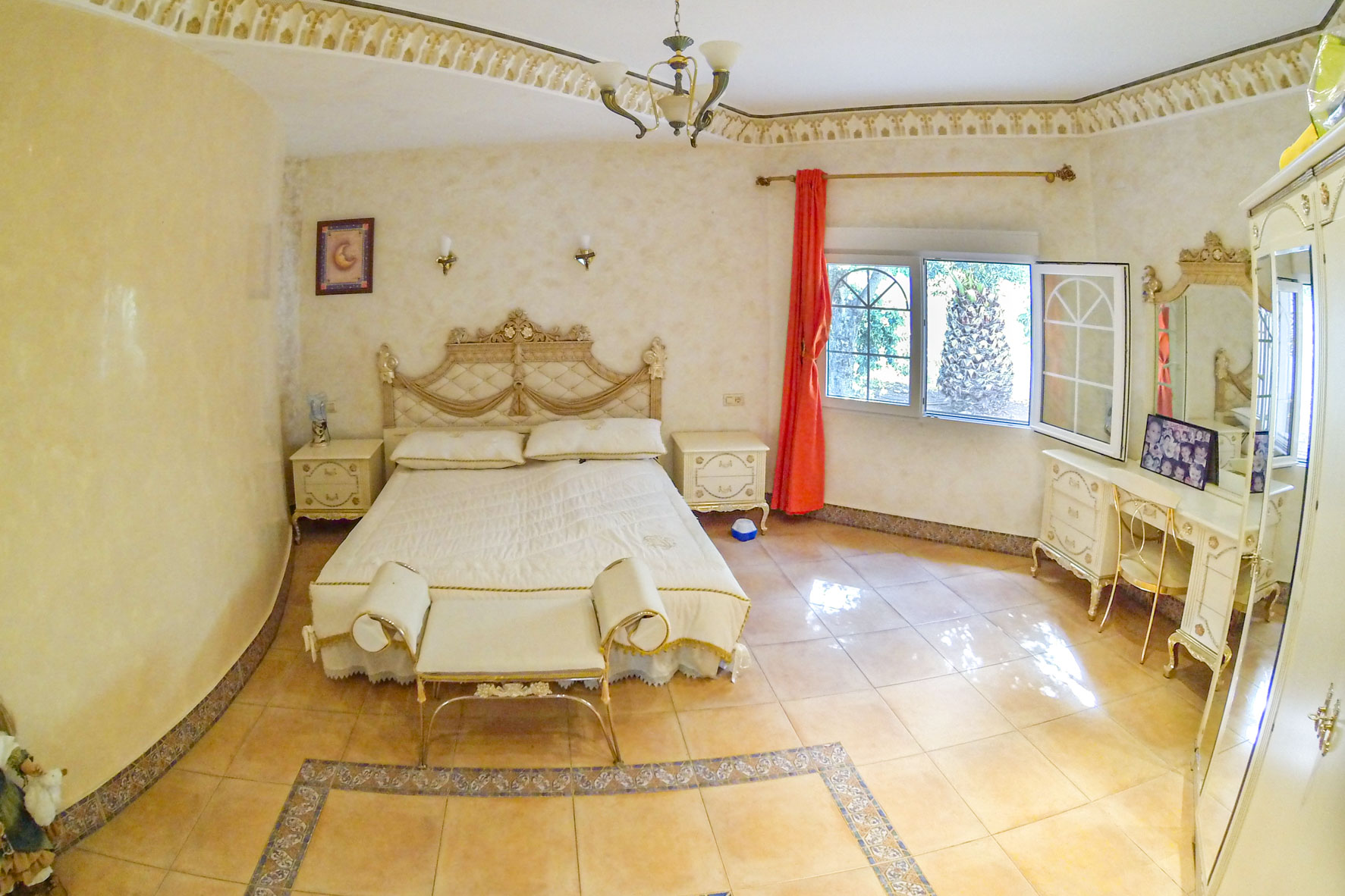 Möbliertes Hauptschlafzimmer mit Doppelbett, Schminktisch und Gartenblick durch ein Fenster.