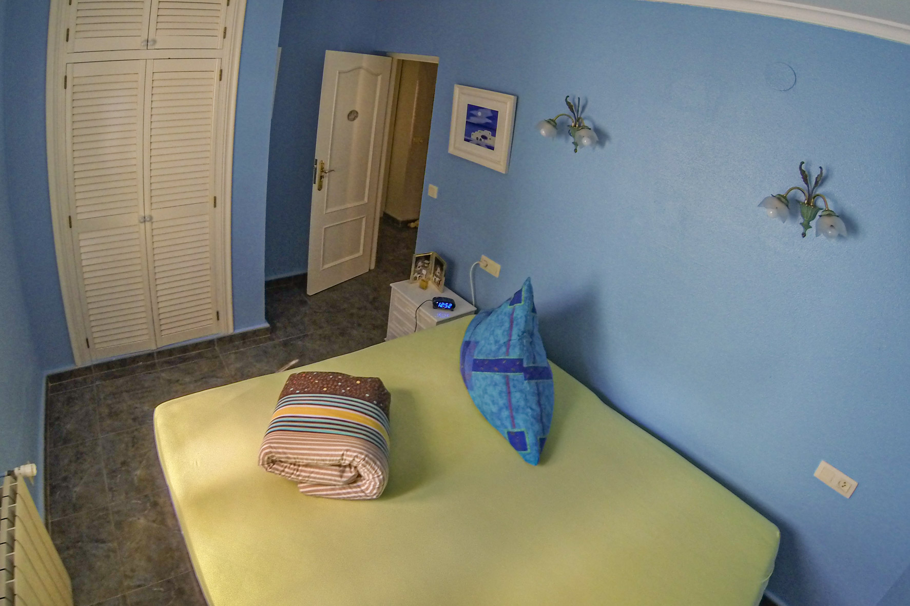 Schlafzimmer mit blauen Wänden, einem Einbauschrank aus weißem Holz und gefalteter Bettwäsche.