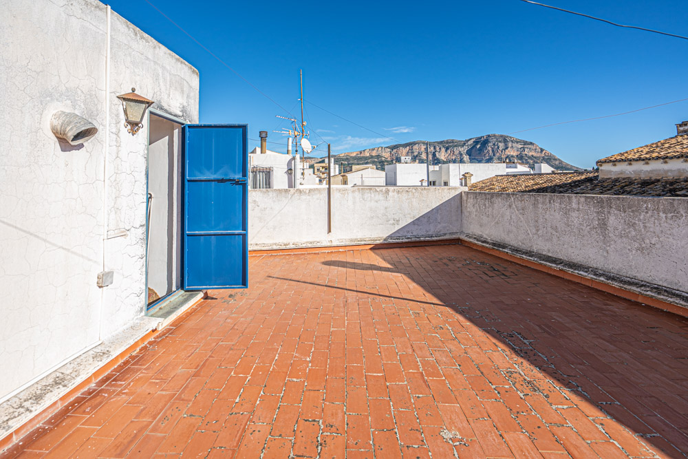 Dachterrasse mit traditionellen Terrakottafliesen, weiß getünchten Mauern und direktem Blick auf das Montgó-Massiv unter blauem Himmel.