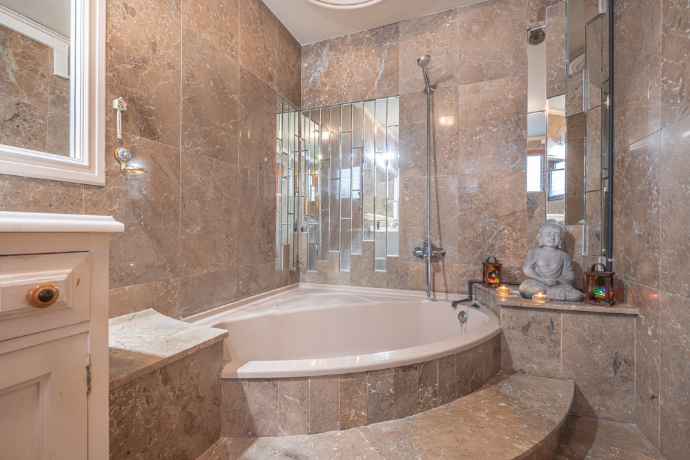 Elegantes Badezimmer mit eingebauter Eckbadewanne, polierten Marmorwänden und einer markanten vertikalen Spiegelanordnung.