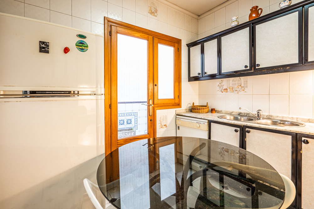 Funktionale Küche mit dunkel abgesetzten Schränken, Marmorarbeitsplatte und einer Glastür aus Holz, die zum Innenhof führt. Inklusive Esstisch mit Glasplatte.