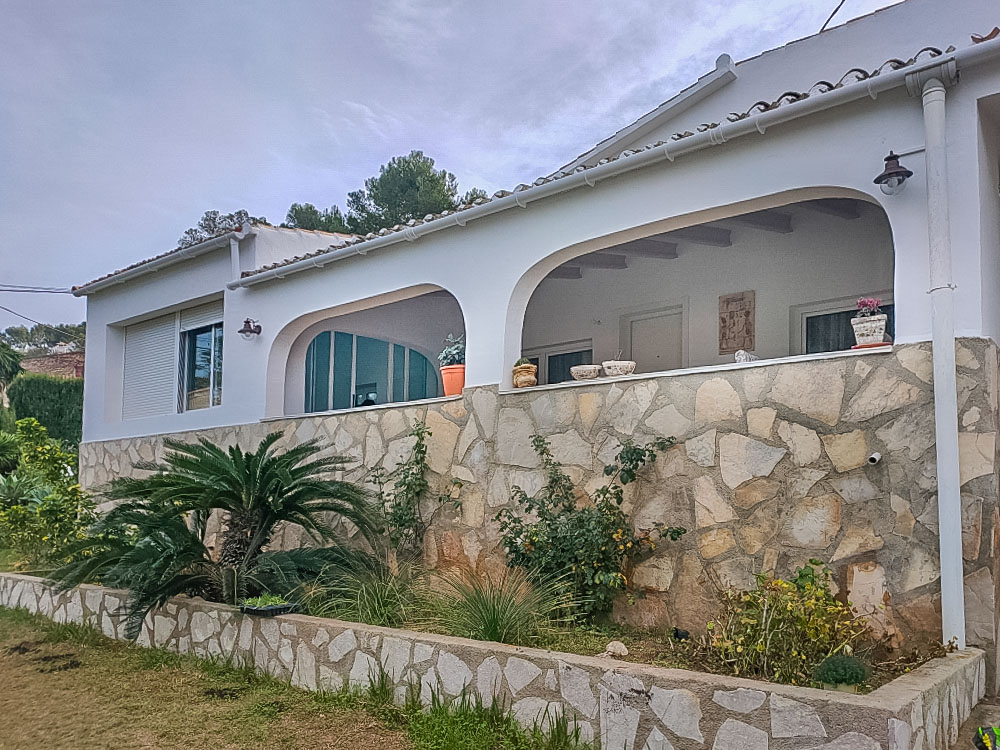 Außenansicht der Villa mit einer traditionellen bogenförmigen Naya und Natursteinmauerwerk. Der Gartenbereich ist mit mediterranen Pflanzen gestaltet.