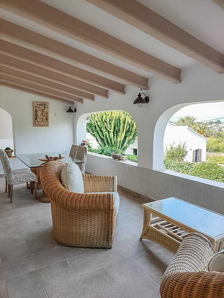 Großzügige überdachte Naya mit Holzbalkendecke, Korbmöbeln und traditionellen Rundbögen mit Blick auf den mediterranen Garten.