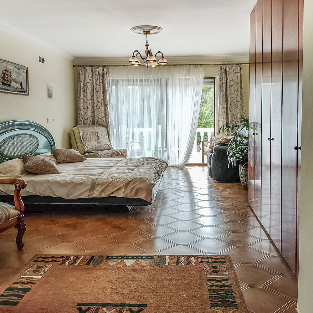 Helles Schlafzimmer mit wandhohen Einbauschränken aus Holz, Fliesenboden mit Rautenmuster und direktem Zugang zur Terrasse durch Glasschiebetüren.