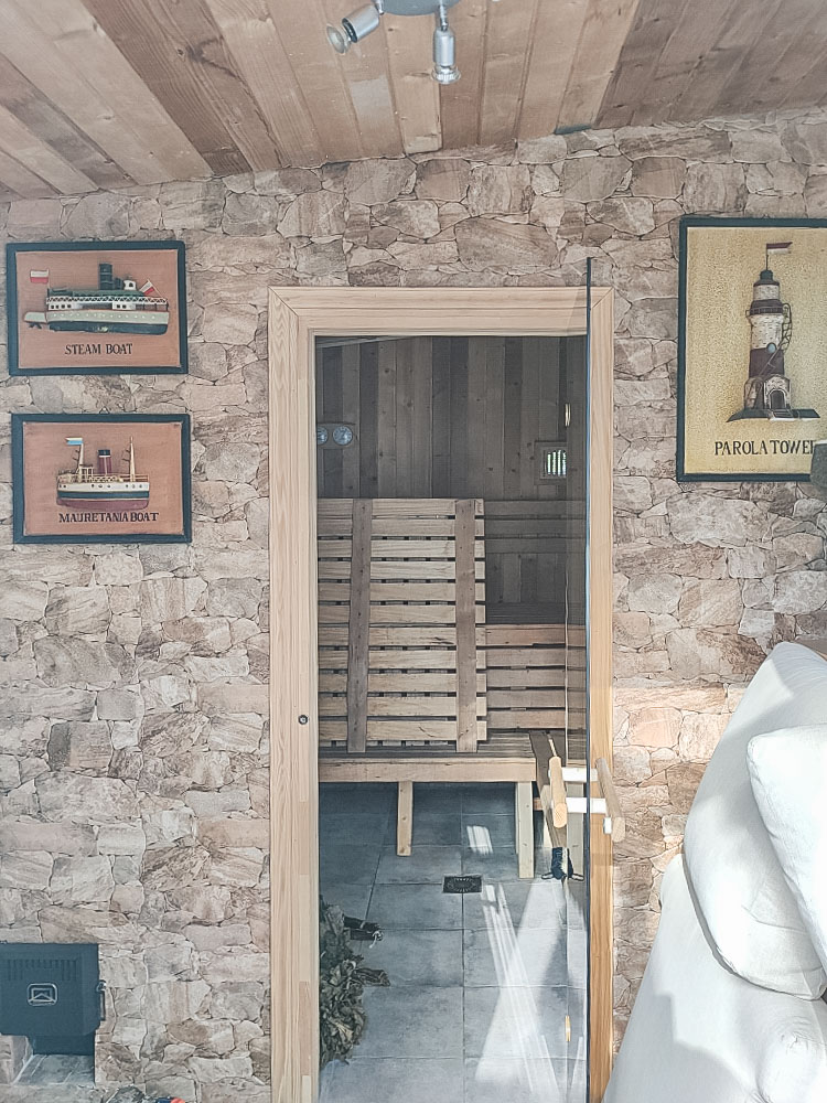 Private Sauna mit Natursteinwänden und Glastür. Der Innenraum ist komplett mit Holz verkleidet und verfügt über mehrstufige Sitzbänke und Messgeräte.