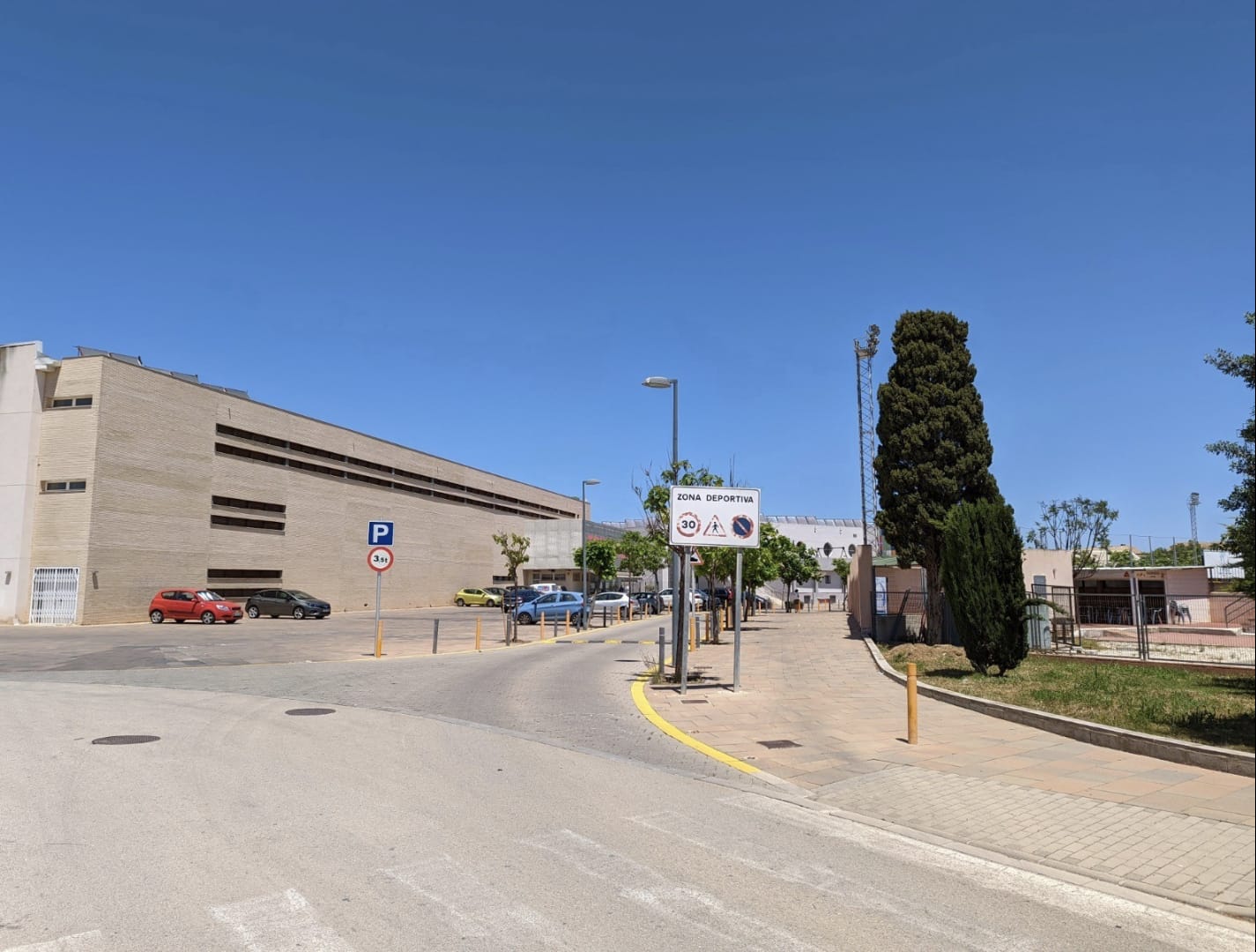Außenansicht der Zufahrt zum Sportzentrum von Denia mit breiten Gehwegen, Verkehrsbeschilderung und modernen institutionellen Backsteingebäuden.