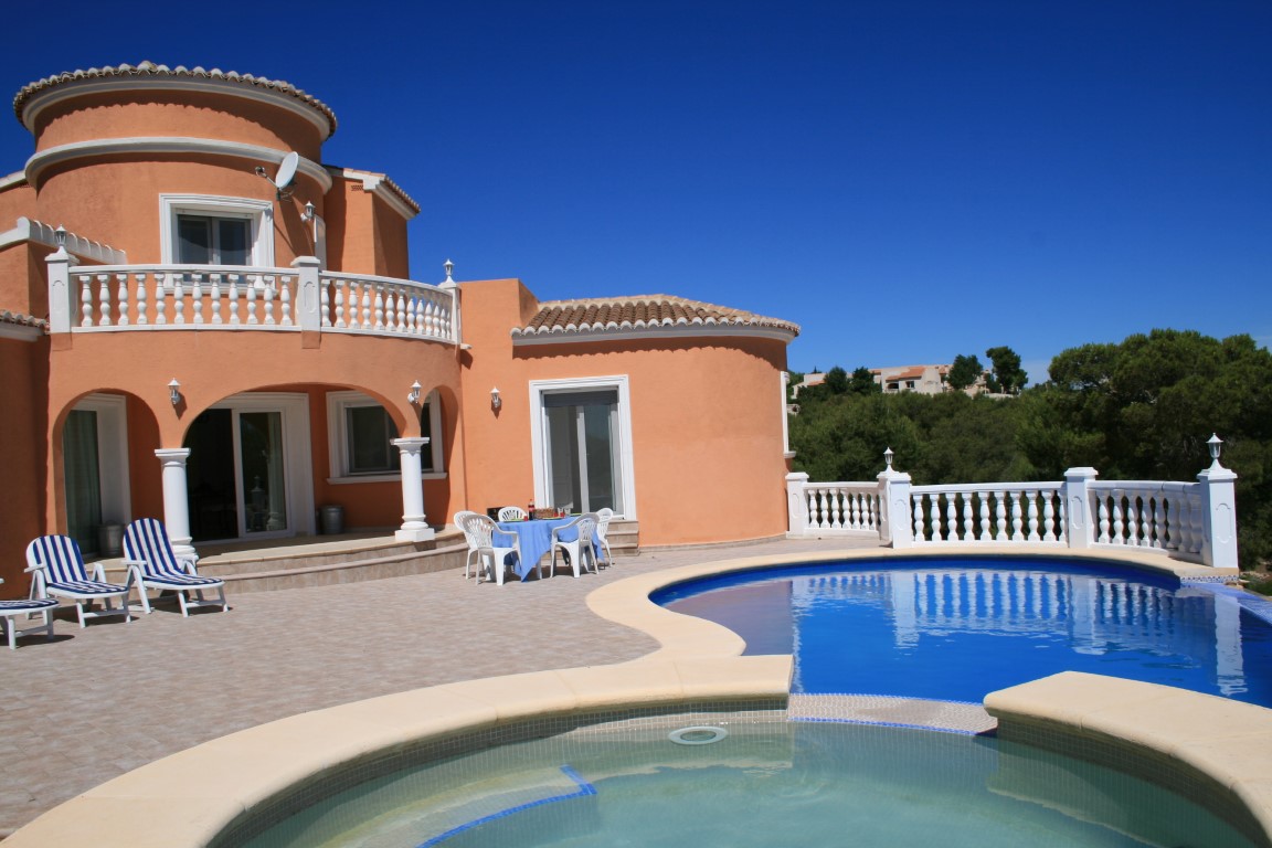 Außenbereich mit geschwungenem Pool, integriertem Jacuzzi, weißen Balustraden und einer terracottafarbenen Villa mit Rundbogen-Veranda und Balkon.