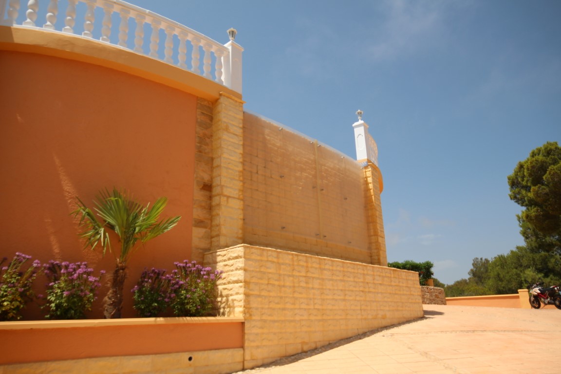Außenmauer aus Tosca-Naturstein und terrakottafarbenem Putz mit Glasschutzwänden, bepflanzten Blumenkästen und einer weißen Balustrade.