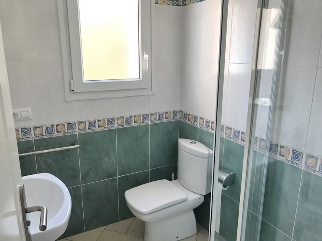Badezimmer mit grün-weißen Wandfliesen, weißem WC, Waschbecken und einer Glasduschkabine. Ein Fenster sorgt für Tageslicht und Belüftung.