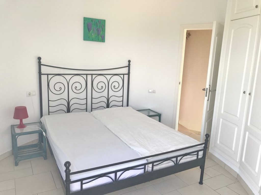 Doppelzimmer mit schwarzem Schmiedeeisenbett, weißen Einbauschränken und hellem Fliesenboden. Die offene Tür führt zum En-Suite-Badezimmer.