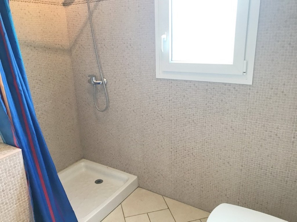 Duschbereich mit beigen Mosaikfliesen, einer weißen Duschwanne und einem Milchglasfenster für natürliches Licht und Privatsphäre.