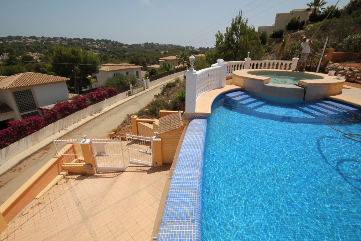 Erhöhter Swimmingpool mit blauen Mosaikfliesen und integriertem runden Whirlpool, eingefasst von einer weißen Balustrade mit Panoramablick.