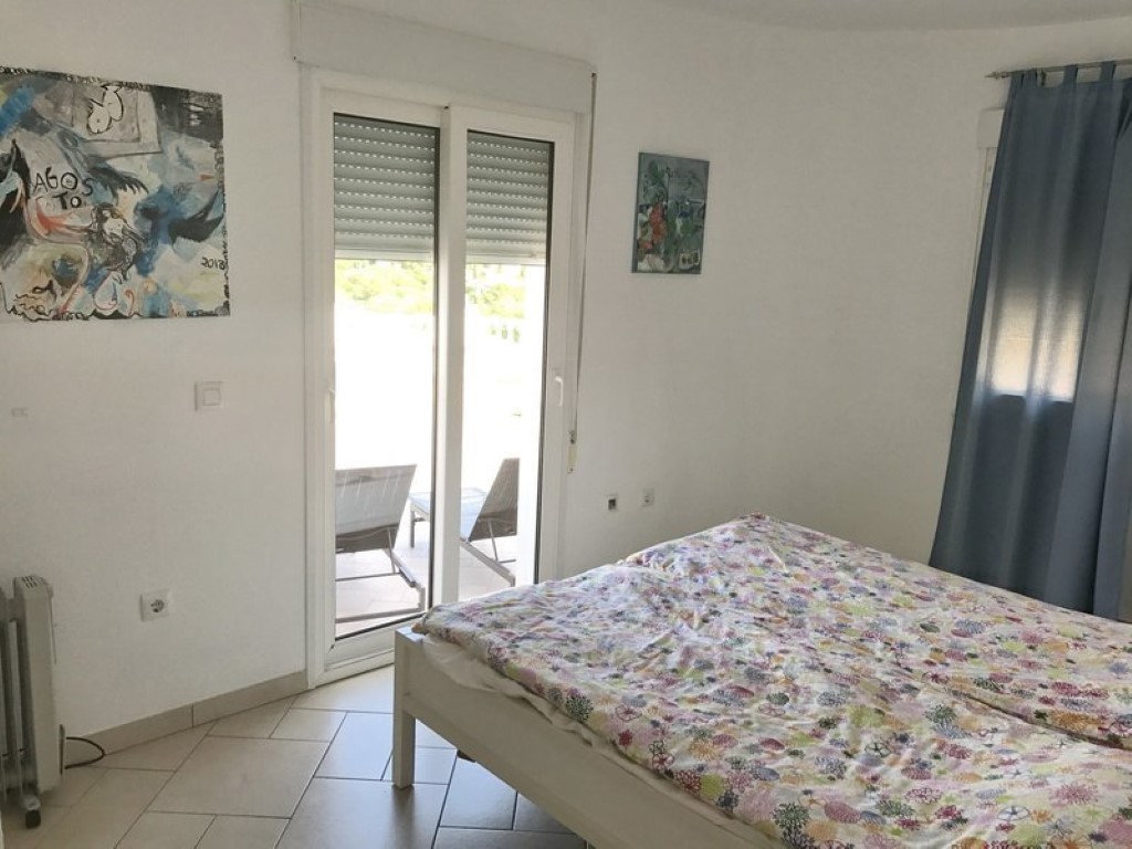 Helles Schlafzimmer mit Fliesenboden und direktem Zugang zur Terrasse durch eine Glasschiebetür, inklusive Blick auf den Außenbereich.