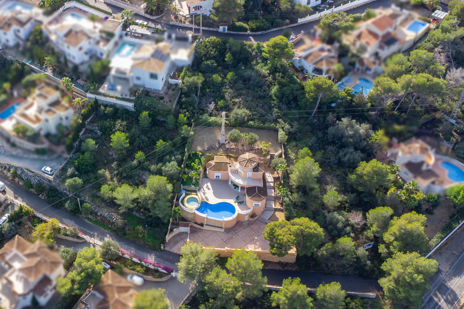 Luftansicht der mediterranen Villa mit nierenförmigem Pool, kreisförmigem Whirlpool und weitläufigen gepflasterten Terrassen inmitten eines Pinienwaldes.