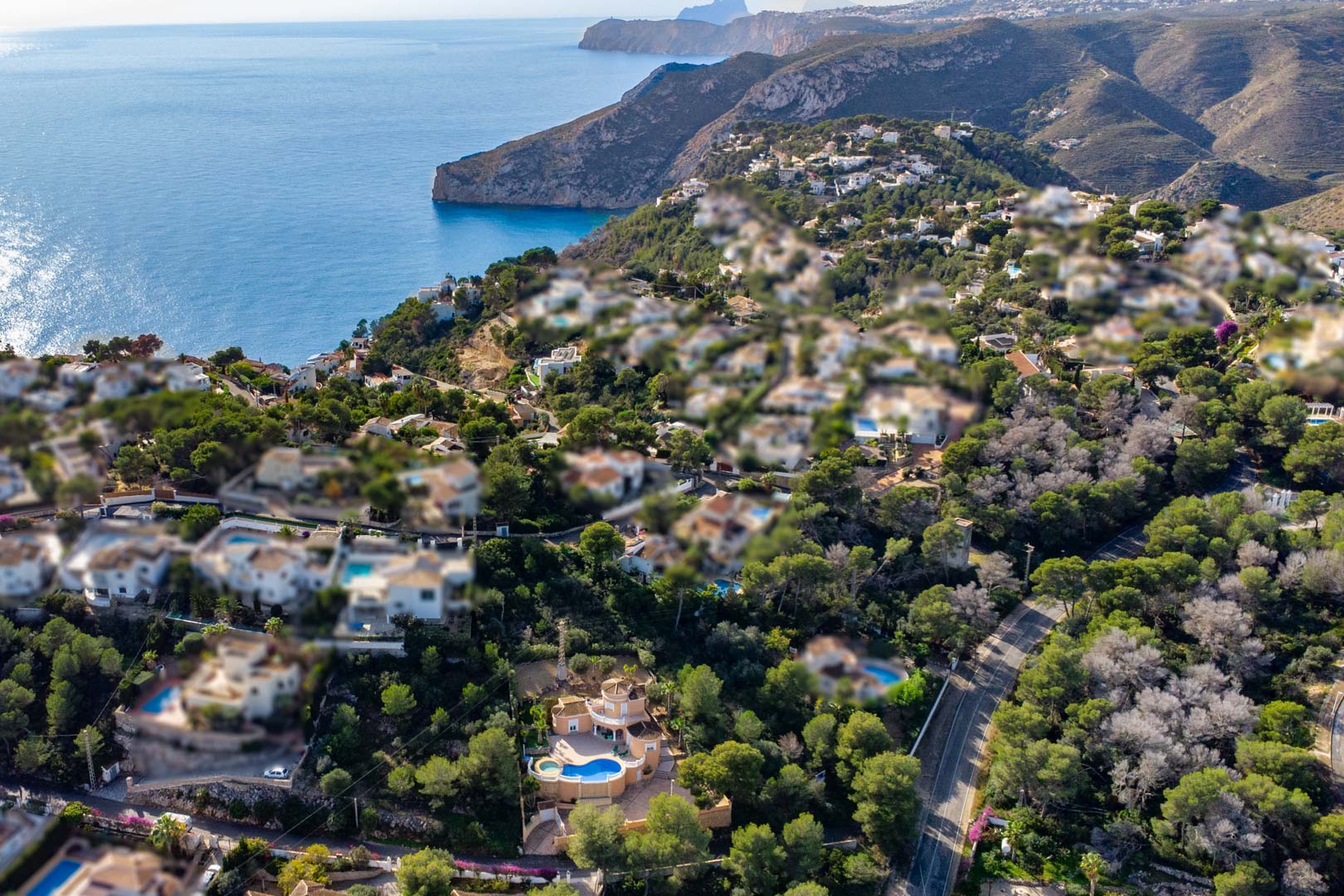 Luftaufnahme der Villa mit geschwungenem Pool und Whirlpool-Bereich, umgeben von Pinien mit weitem Panoramablick auf das Mittelmeer und die Küste von Javea.