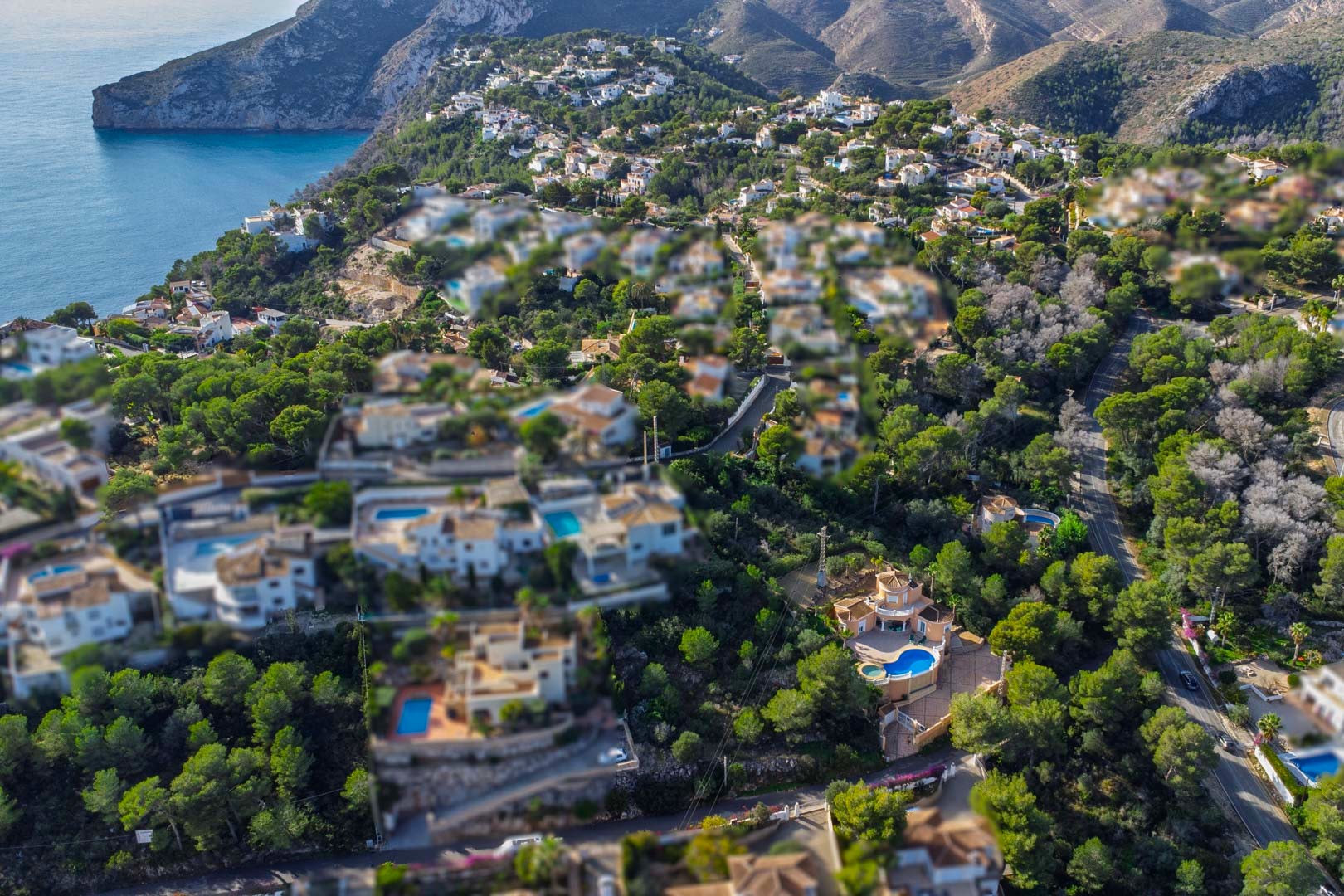 Luftaufnahme eines Wohngebiets in Javea mit mediterranen Villen und privaten Pools, umgeben von Pinienwäldern nahe der Küste und den Klippen.