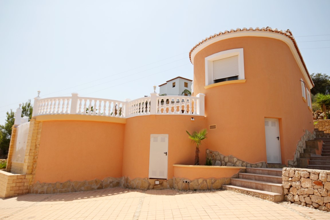 Mediterrane Villa mit terracottafarbenem Rundturm, weißer Balustrade und gepflastertem Außenbereich mit Natursteintreppen.