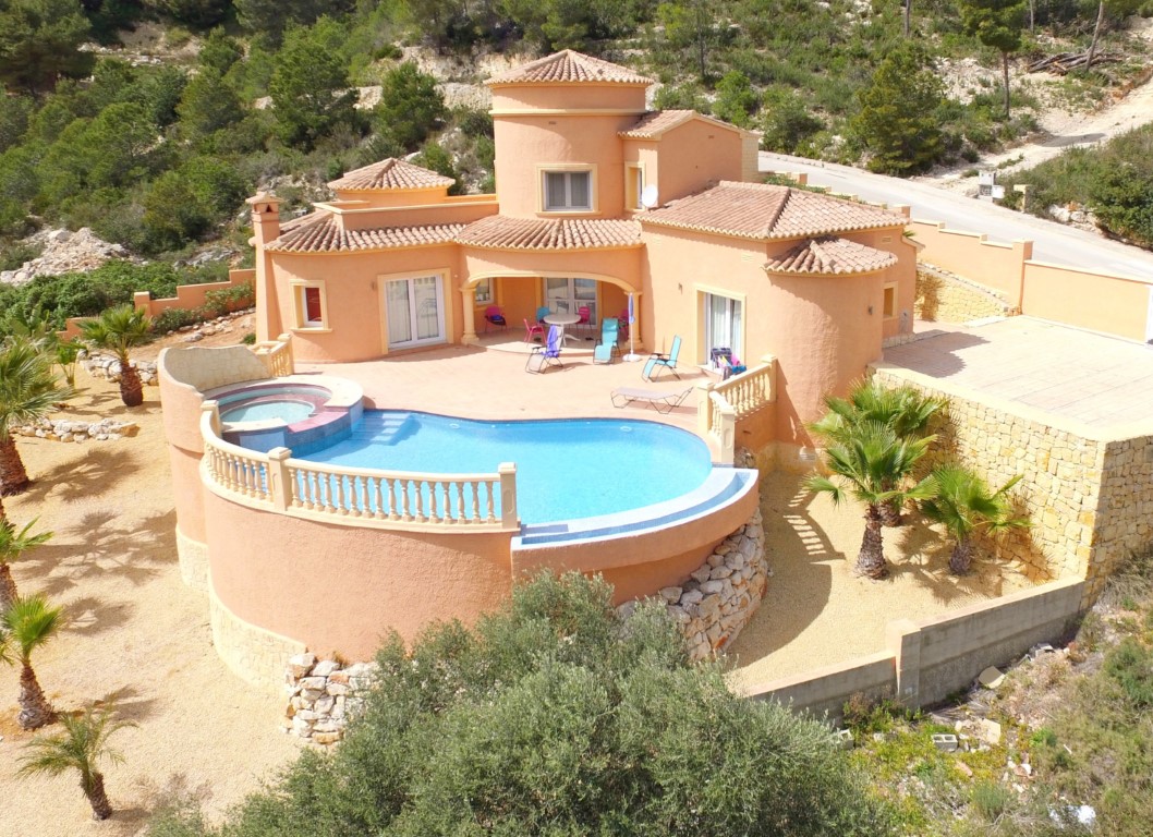 Außenansicht der mediterranen Villa mit geschwungenem Infinity-Pool, integriertem Whirlpool und weitläufiger Terrasse mit Palmen.