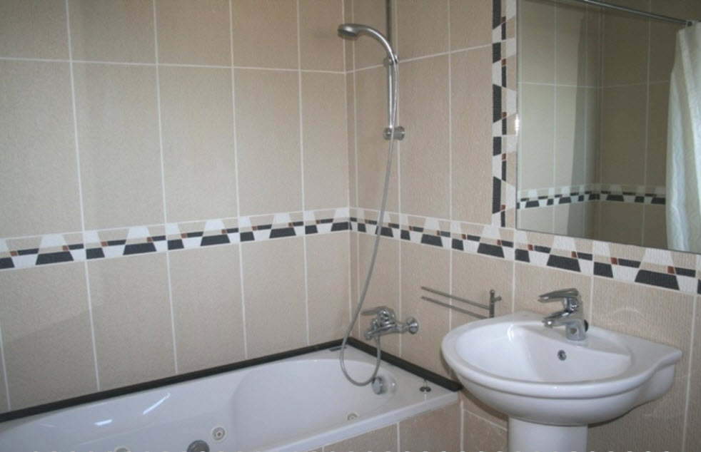 Badezimmer mit Hydromassage-Badewanne, Standwaschbecken und beigefarbenen Wandfliesen mit dekorativer geometrischer Bordüre.