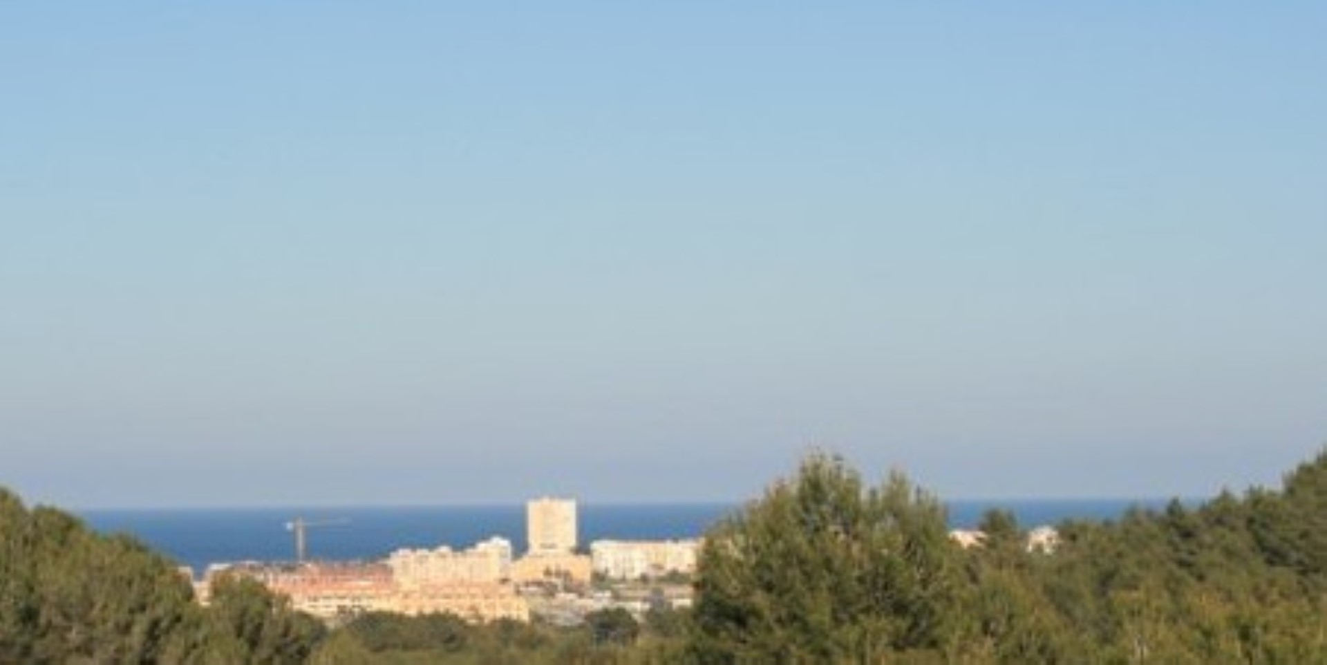 Erhöhter Panoramablick auf das Mittelmeer und die Küstenbebauung, eingebettet in eine natürliche Umgebung mit Pinienbäumen.