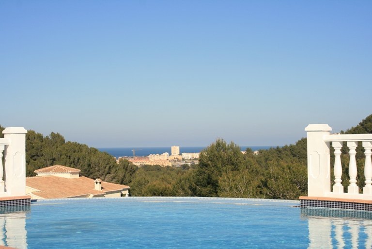 Infinity-Pool mit blauem Mosaik und weißer Balustrade, mit weitem Blick über Pinienwälder bis hin zum Mittelmeer und der Küste von Jávea.