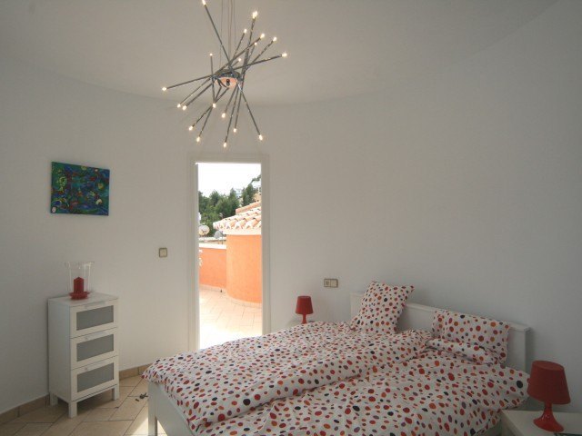 Schlafzimmer mit geschwungenen Wänden, modernem Design-Leuchter und direktem Zugang zur privaten Dachterrasse.