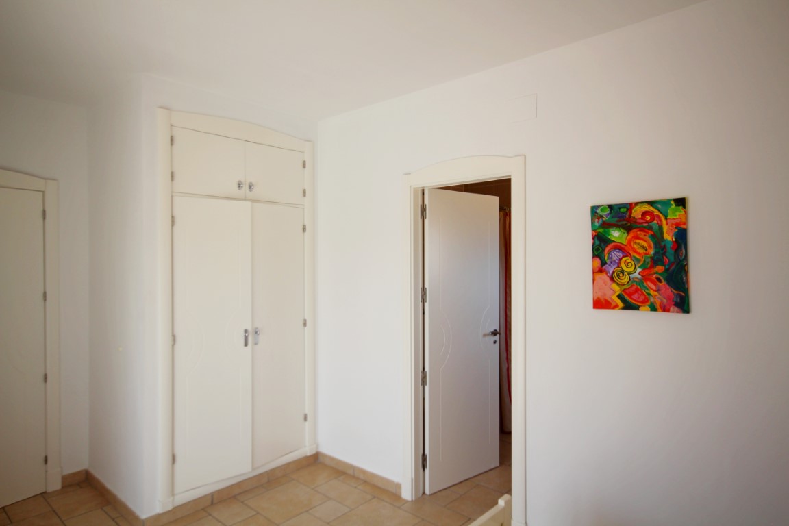 Schlafzimmer mit weißem Einbauschrank, Terrakotta-Fliesenboden und hellen Wänden, ergänzt durch ein farbenfrohes abstraktes Bild.