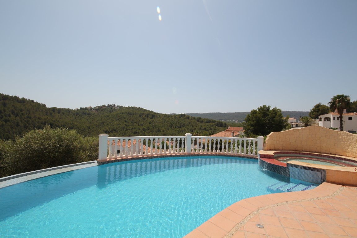 Sonnenterrasse mit geschwungenem Infinity-Pool, integriertem Whirlpool und Panoramablick auf die bewaldeten Hügel der Umgebung.