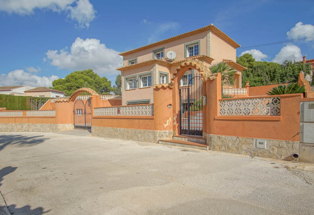 Außenansicht der dreistöckigen Villa mit terrakottafarbenen Wänden, Natursteinsockel und zwei bogenförmigen Schmiedeeisentoren für Fußgänger und Fahrzeuge.