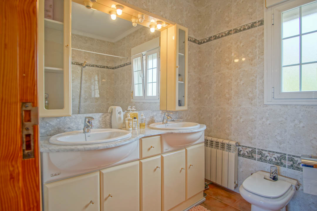 Badezimmer mit Doppelwaschbecken auf Marmorplatte, beleuchtetem Spiegelschrank und klassisch gefliesten Wänden mit dekorativer Bordüre.