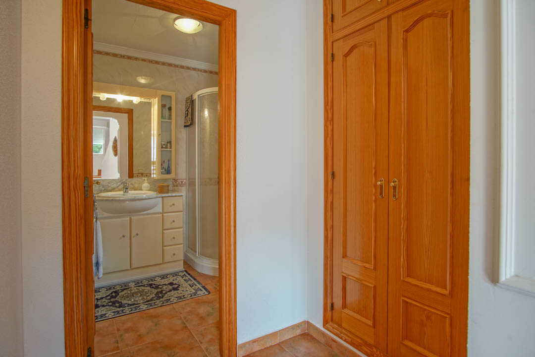 Einbauschrank aus Massivholz neben einem Badezimmer mit Marmorwaschtisch, Eckdusche und zeitlosen Keramikfliesen.
