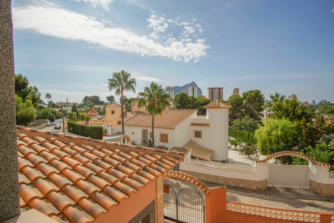 Erhöhte Aussicht vom Obergeschoss auf die traditionellen Ziegeldächer, die mediterrane Nachbarschaft mit Palmen und den Peñón de Ifach am Horizont.