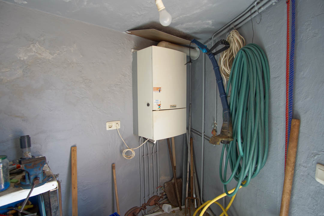 Funktionaler Abstellraum mit Vaillant-Gastherme, Werkbank mit Schraubstock und Lagerfläche für Gartengeräte und Schläuche.