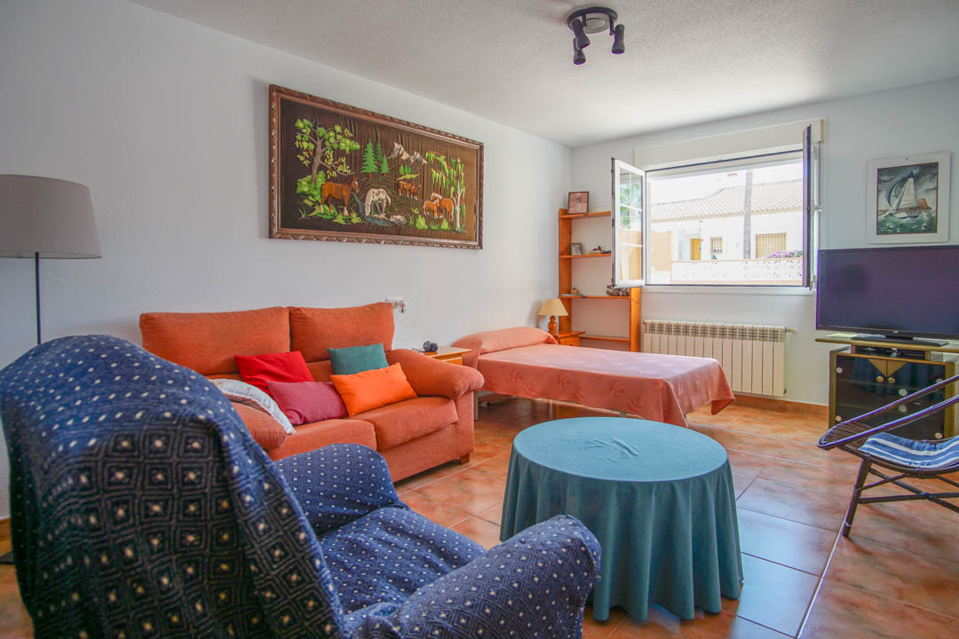 Funktionaler Wohnbereich mit Keramikfliesen, Sitzecke, Einzelbett und einem großen Fenster, das den Raum mit natürlichem Licht durchflutet.