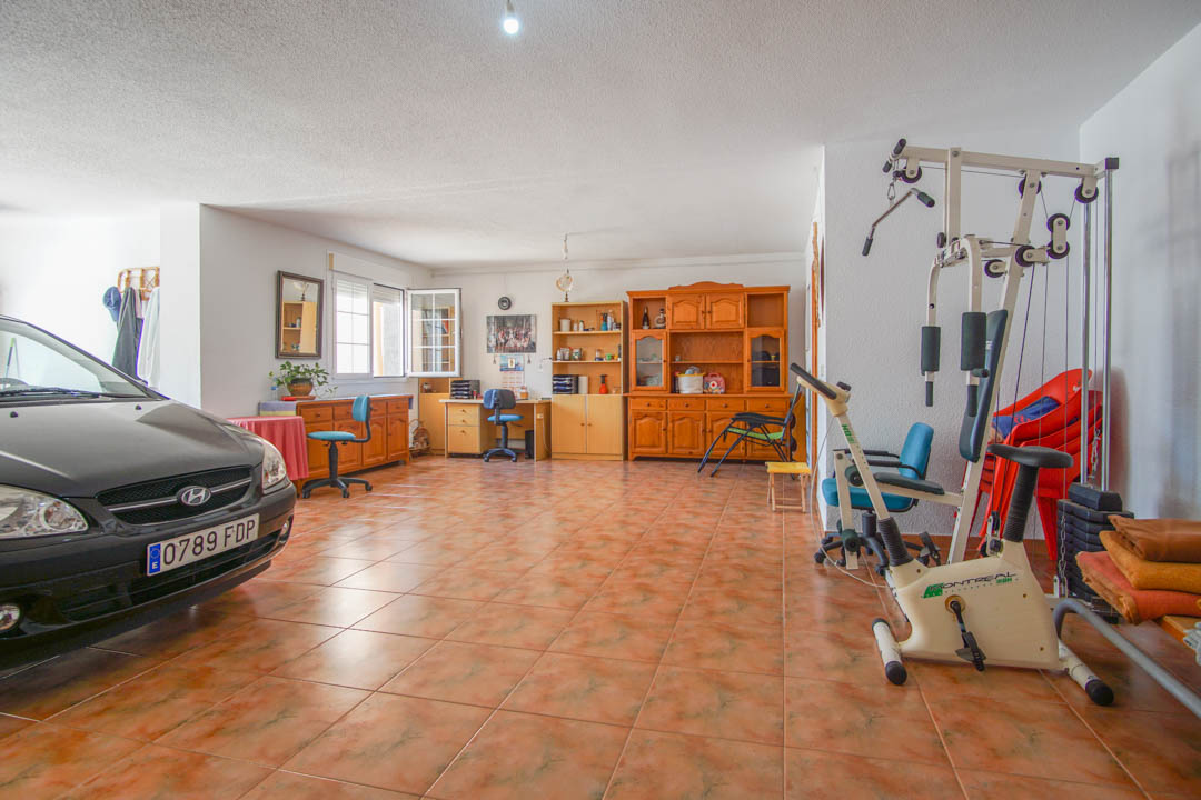 Geräumige Garage im Erdgeschoss mit Fliesenboden, ausgestattet mit Massivholzmöbeln, einem Fitnessbereich und einem hellen Büroarbeitsplatz.