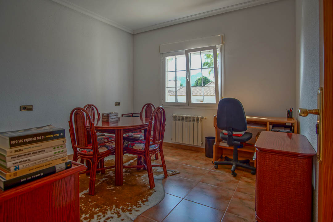 Hell eingerichtetes Arbeitszimmer mit Fliesenboden, Massivholztisch und Schreibtischbereich. Das Fenster sorgt für natürliches Licht und Ausblick auf die Umgebung.